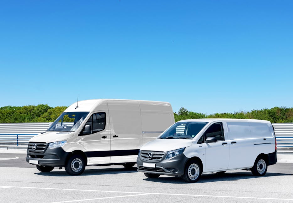 Two white Mercedes-Benz cargo vans parked side by side on a paved surface beneath a clear blue sky. The larger van on the left is positioned parallel to a metal guardrail, with the front facing slightly to the right, and features a high roof, black bumper, and side mirrors. The smaller van on the right is parked closer to the camera, with its front facing forward and slightly to the left, displaying a lower roofline and similar black detailing on the grill and bumper. Both vehicles are part of a house removal or relocation fleet utilized by Man with Van Ardleigh Green, situated in an outdoor area with visible greenery in the background. The scene suggests a loading or parking area near a property, aligned with moving logistics processes such as furniture transport, packing, and loading during a home relocation, supporting services dedicated to removals.