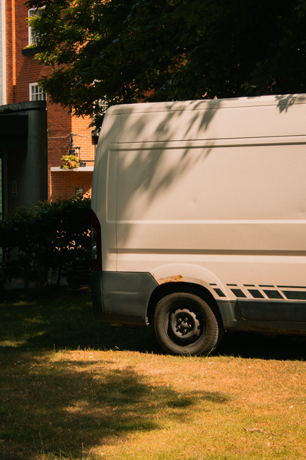 Close-up image of a white delivery van parked outdoors, with the company slogan 'Delivery Always on Time' prominently displayed in large, dark blue letters on the side panel. The van appears to be part of a professional removals service, with a focus on reliable furniture transport and home relocation. The background features blurred green foliage and hints of sky, indicating daylight conditions. The van's surface is clean and reflective, emphasizing a well-maintained vehicle used for packing and moving logistics. Inside the image, no personnel or objects are visible, solely the branding and exterior of the van, which aligns with the theme of professional house removals and transport services provided by Man with Van Ardleigh Green, especially relevant to navigating house removal permits or parking regulations for Ardleigh Green relocations.